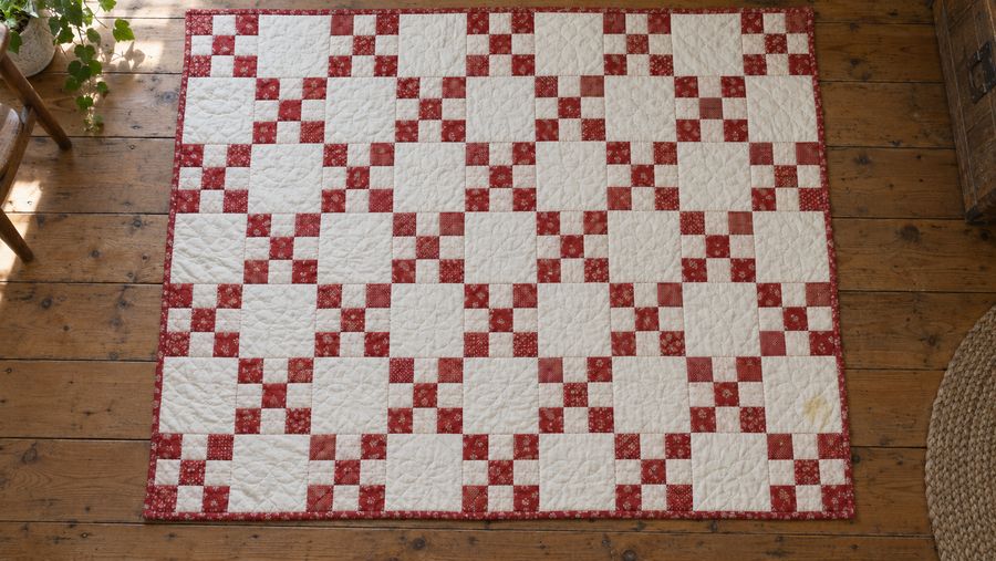 A red and white Nine Patch quilt laid out on a wooden floor